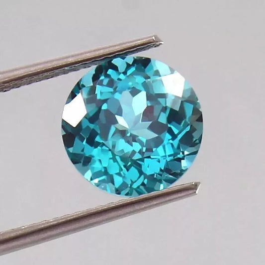 Parti Sapphire gemstone held between tweezers on a light gray background