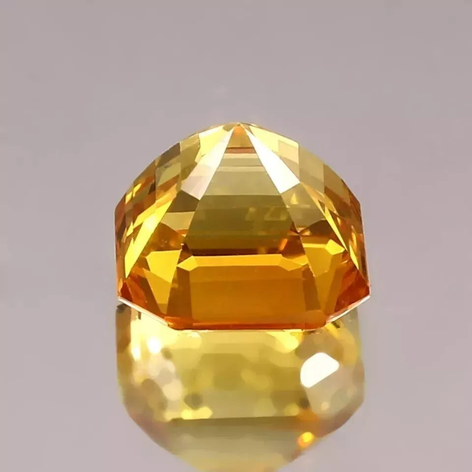 Faceted Ceylon Yellow Sapphire gemstone on a reflective surface with a gray background