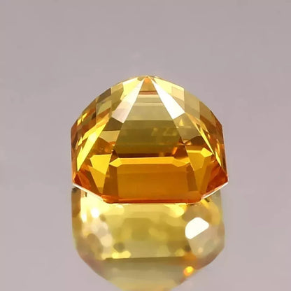 Faceted Ceylon Yellow Sapphire gemstone on a reflective surface with a gray background
