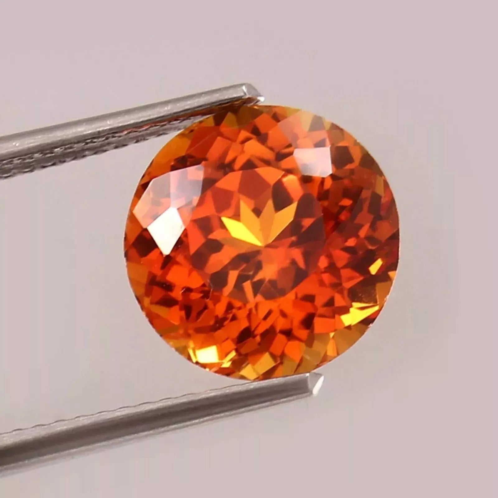 Orange Sapphire gemstone held between tweezers on a light gray background