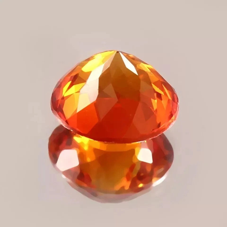 Faceted Orange Sapphire gemstone on a reflective surface with a neutral background