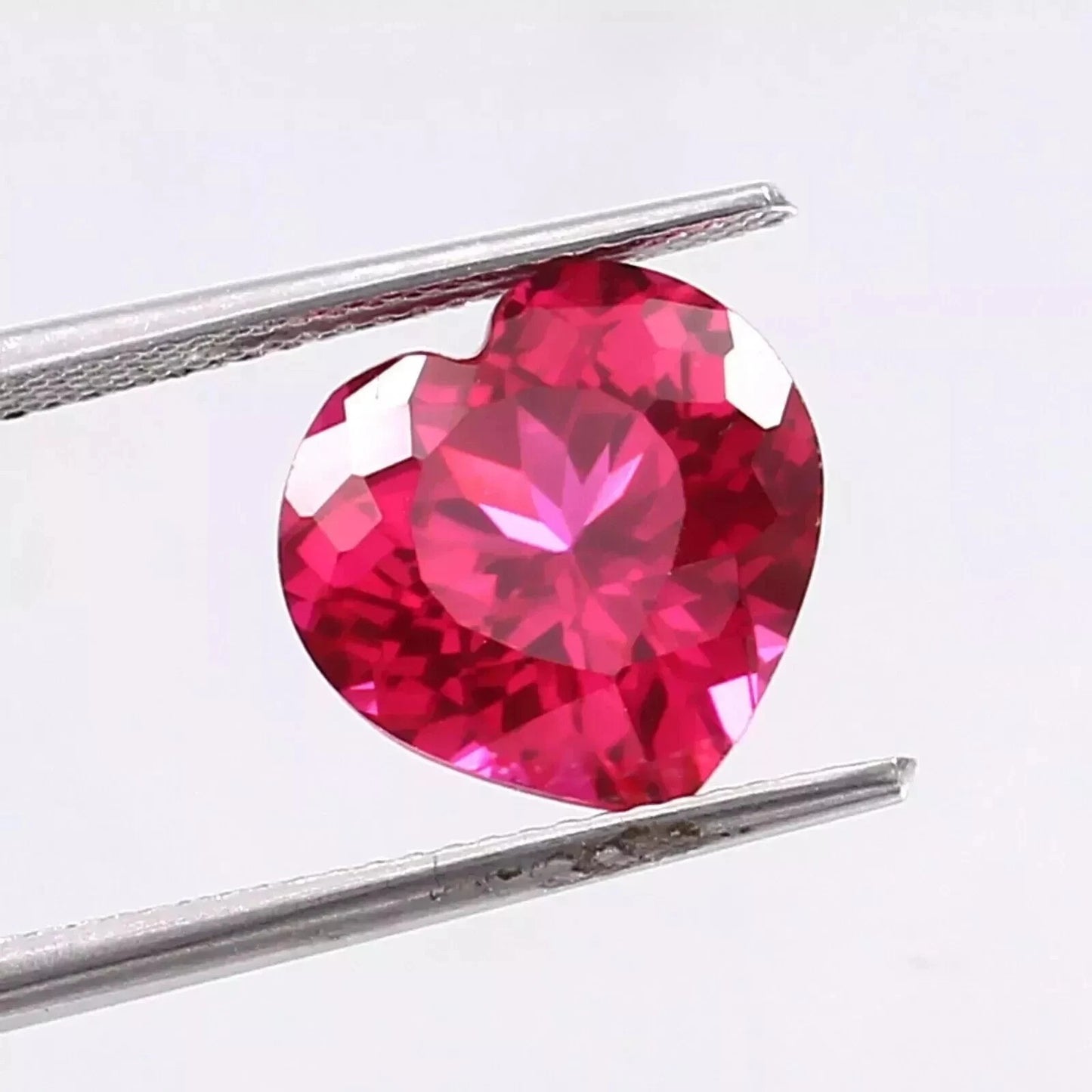Heart-shaped Pink Ruby gemstone held between tweezers on a white background