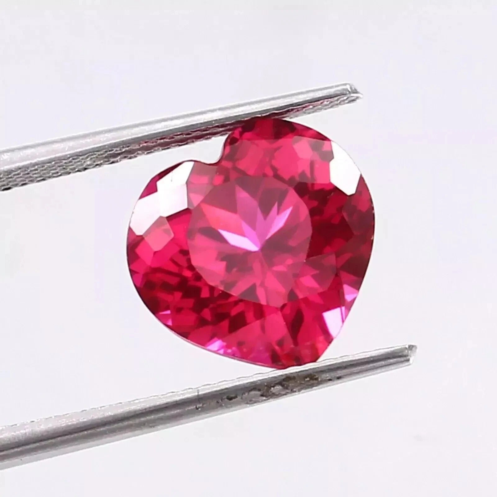 Heart-shaped Pink Ruby gemstone held between tweezers on a white background