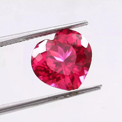 Heart-shaped Pink Ruby gemstone held between tweezers on a white background