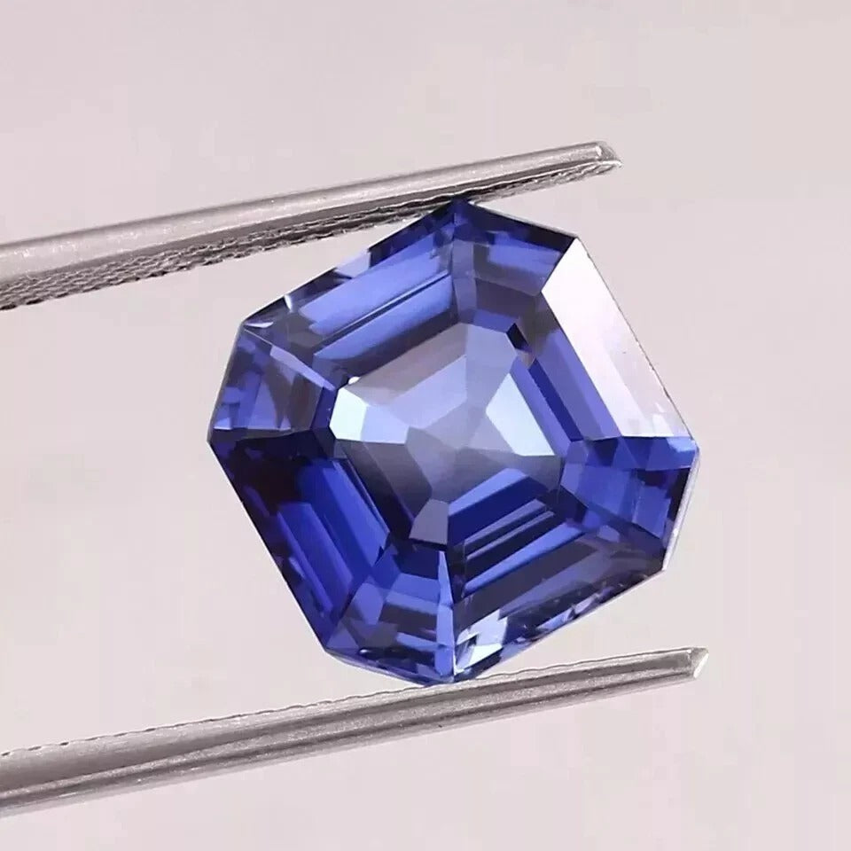Royal Blue Sapphire gemstone held by tweezers on a light gray background