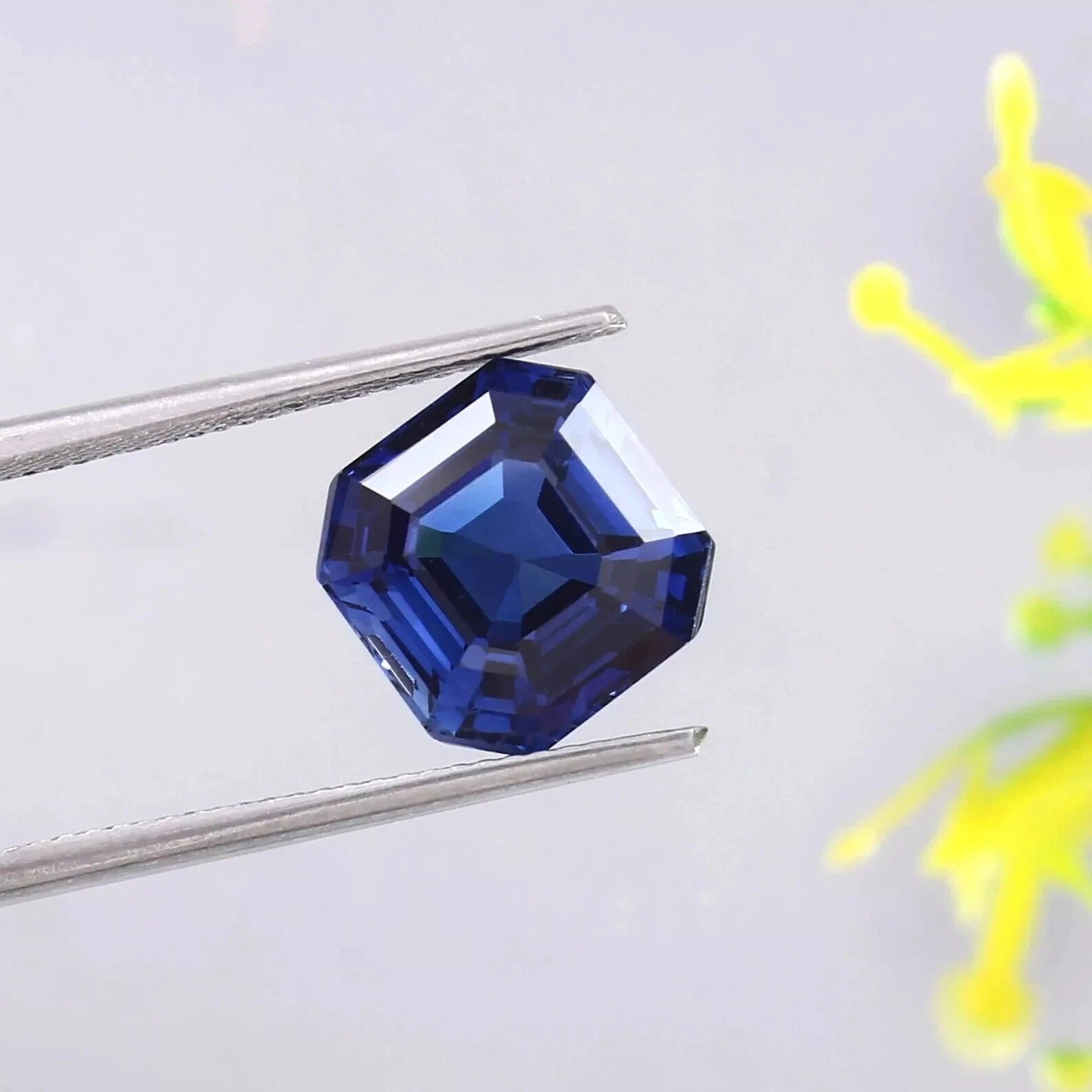 Blue Sapphire gemstone held by tweezers on a light gray background