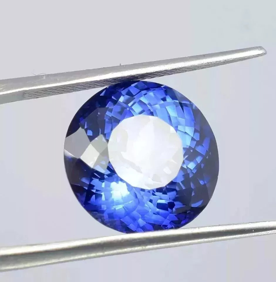 Royal Blue Sapphire gemstone held by tweezers against a light gray background