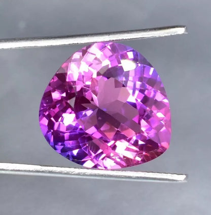 Purple Blue Sapphire gemstone held between tweezers on a gray background