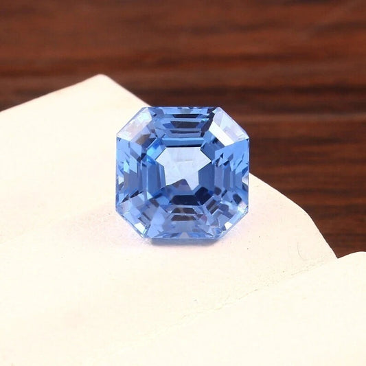 Blue Spinel gemstone on a white surface with a wooden background