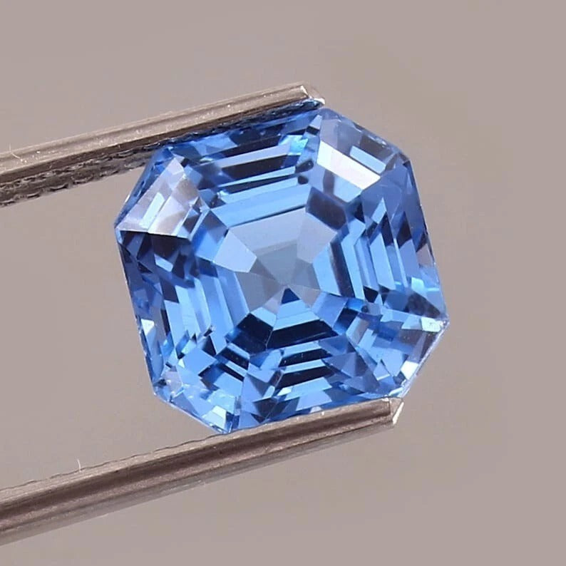 Blue Spinel gemstone held by tweezers on a neutral background