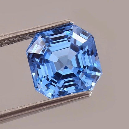 Blue Spinel gemstone held by tweezers on a neutral background