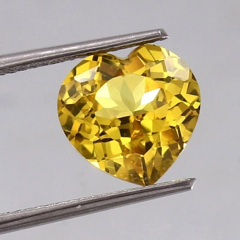 Heart-shaped Yellow Sapphire gemstone held between tweezers against a gray background