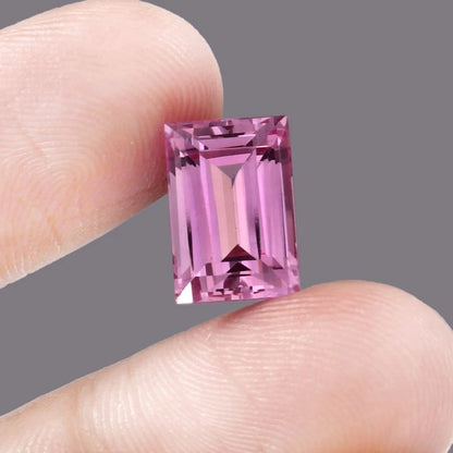 Pink Baguette Cut sapphire gemstone held between two fingers against a gray background