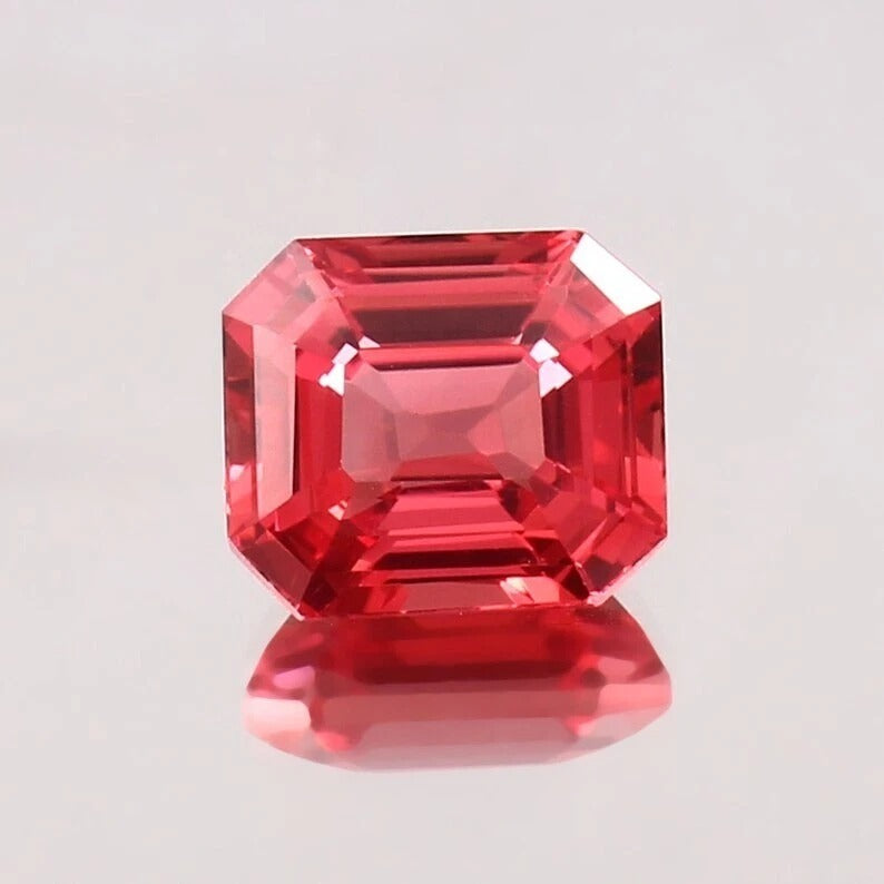 Padparadscha Sapphire gemstone with an emerald cut on a light gray background