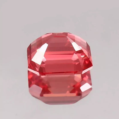 Faceted Padparadscha Sapphire gemstone on a gray background