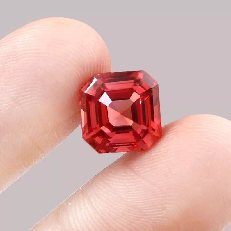 Padparadscha Sapphire gemstone held between fingers against a neutral background
