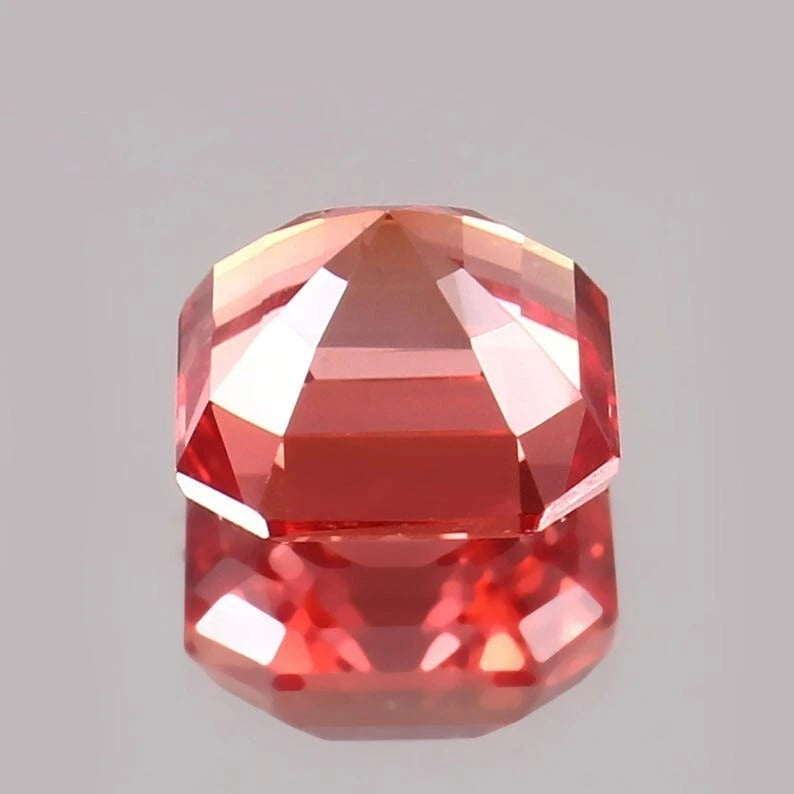 Faceted Padparadscha Sapphire gemstone on a gray background