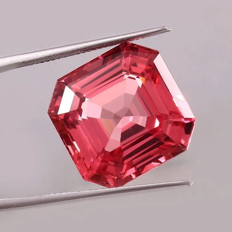 Padparadscha Sapphire gemstone held by tweezers on a gray background