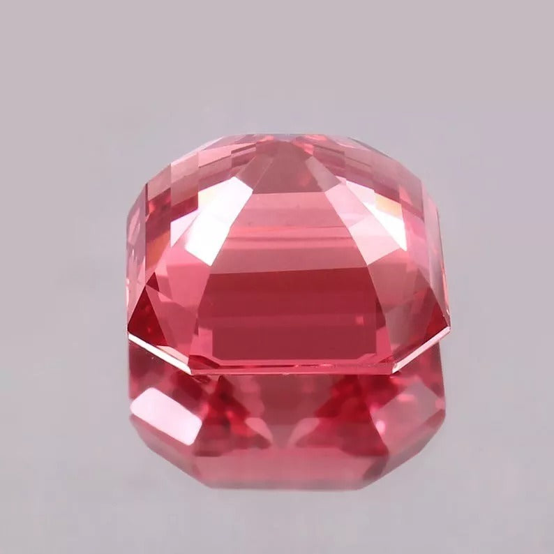 Faceted Padparadscha Sapphire gemstone on a gray background