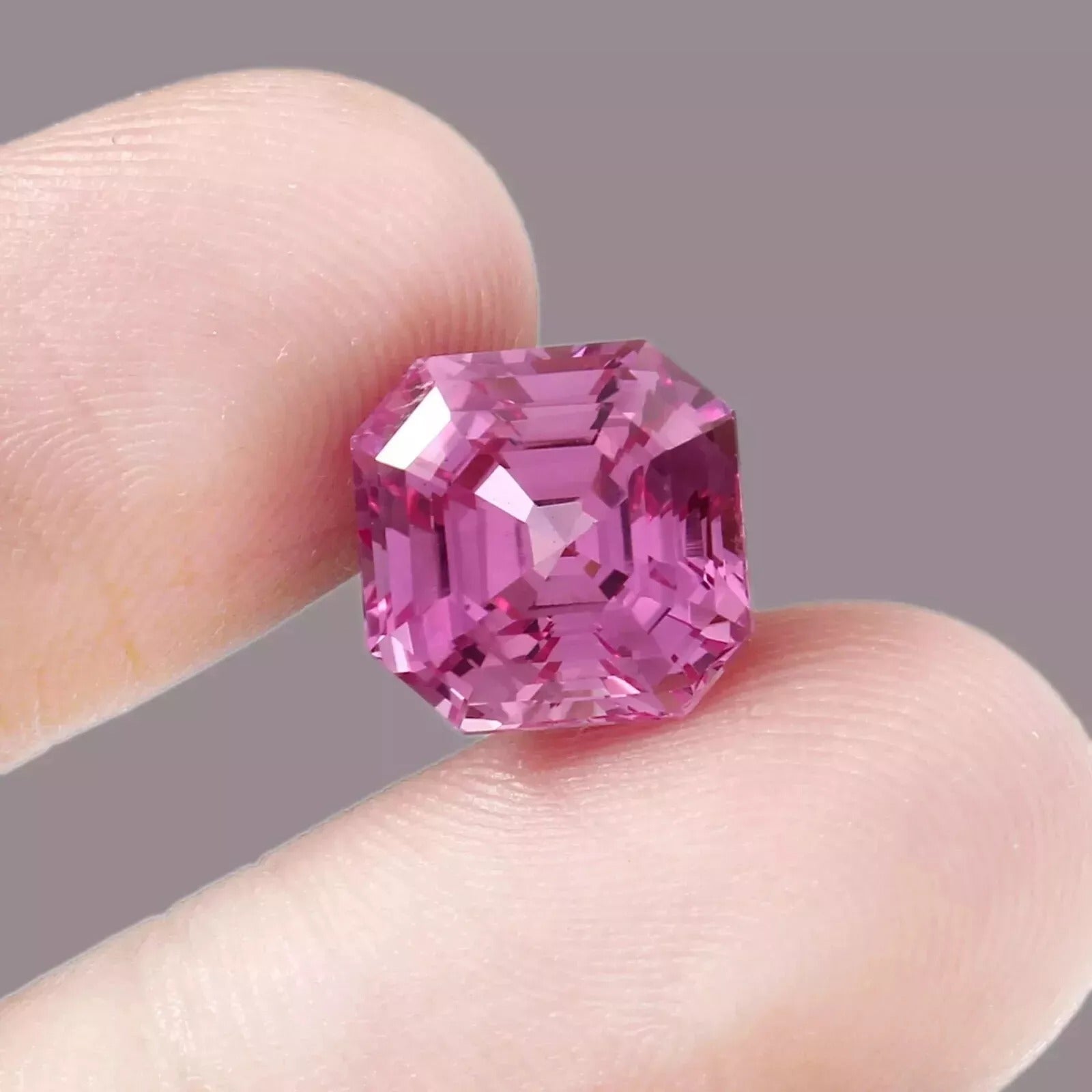 Ceylon Pink Sapphire gemstone held between two fingers against a neutral background
