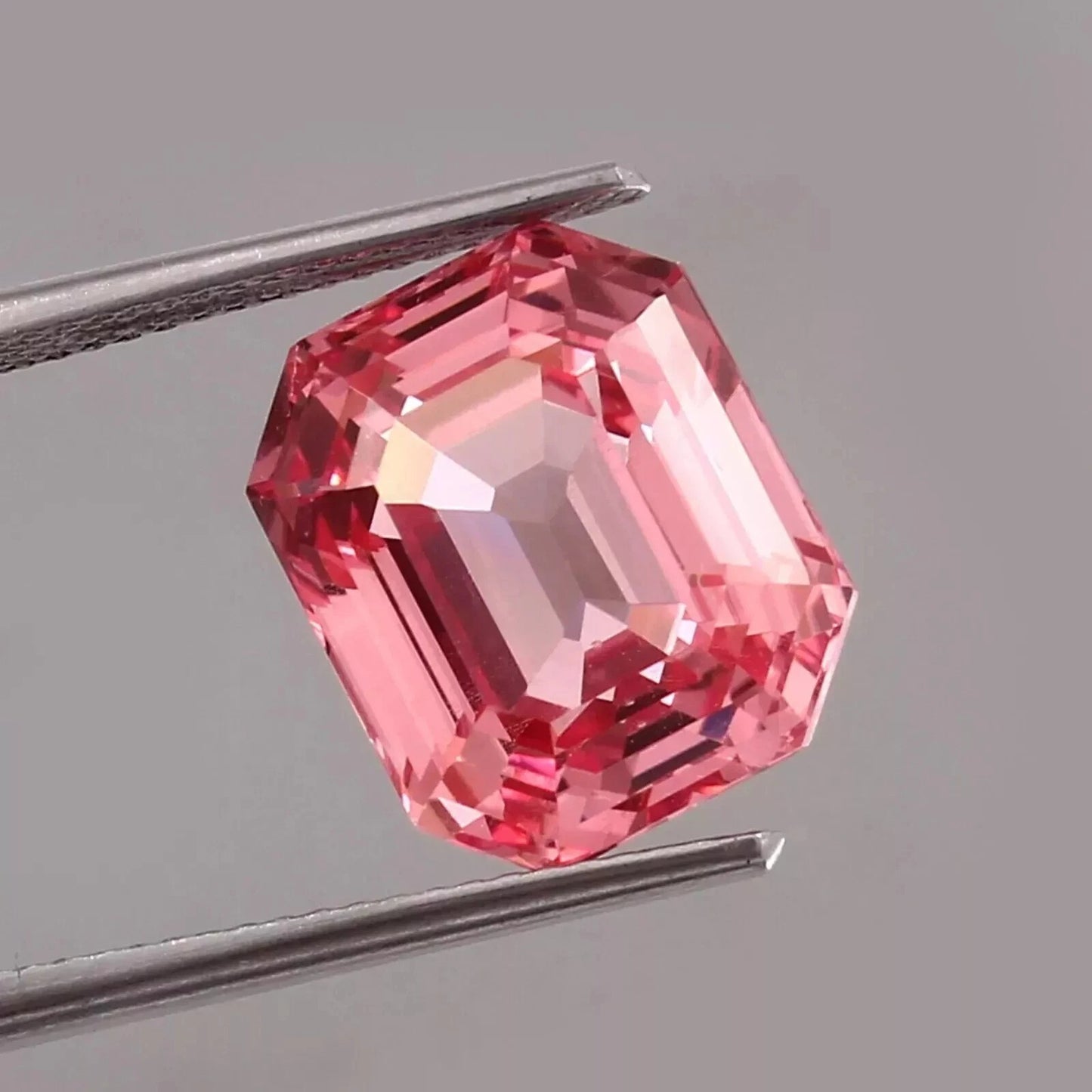 Padparadscha Sapphire Pink gemstone held by tweezers on a gray background