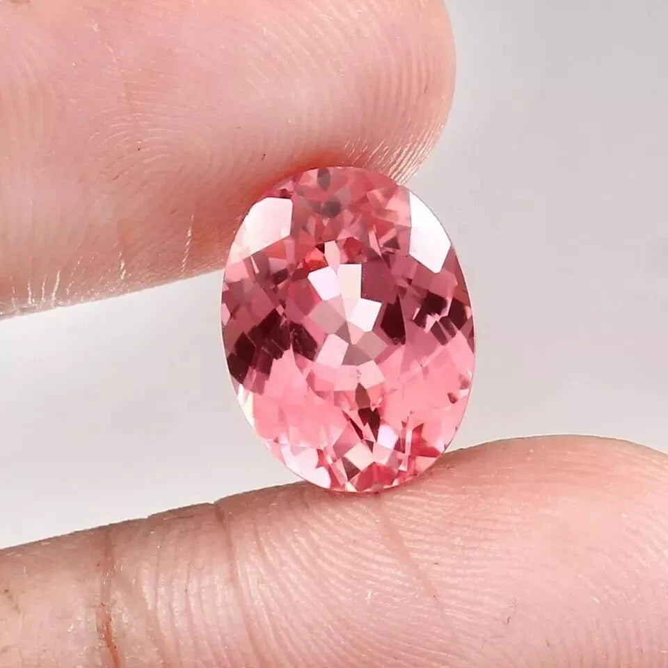 Padparadscha Sapphire Peach To Pink gemstone held between fingers against a neutral background