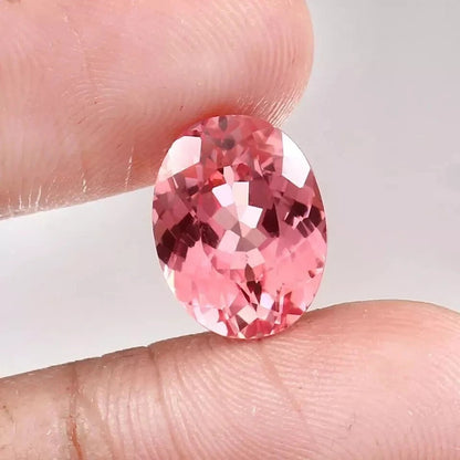 Padparadscha Sapphire Peach To Pink gemstone held between fingers against a neutral background