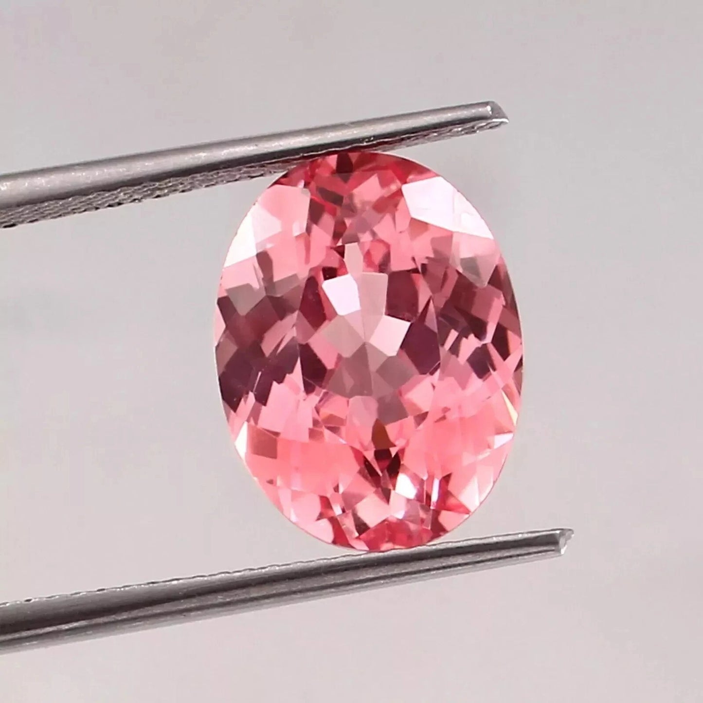 Padparadscha Sapphire Peach To Pink gemstone held by tweezers on a light gray background