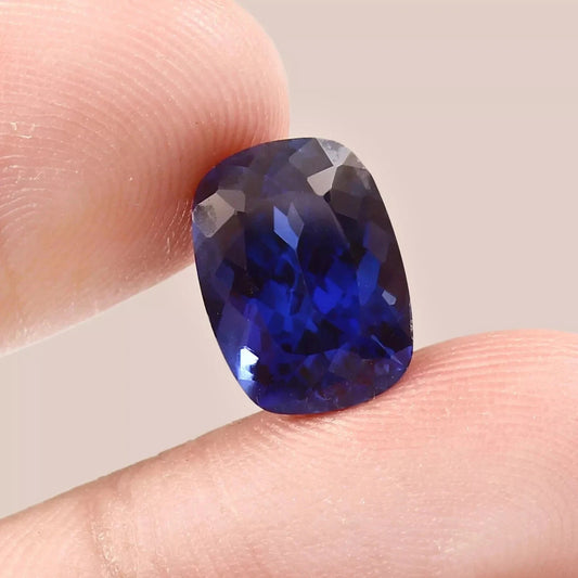 Faceted Blue Sapphire gemstone held between fingers against a neutral background
