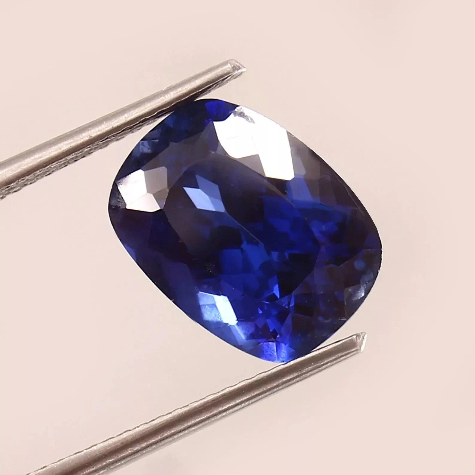 Blue Sapphire gemstone held between tweezers on a beige background