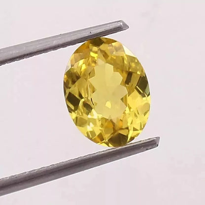 Yellow Sapphire gemstone held between tweezers against a light gray background