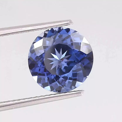 Royal Blue Sapphire Round Cut gemstone held by tweezers on a light gray background