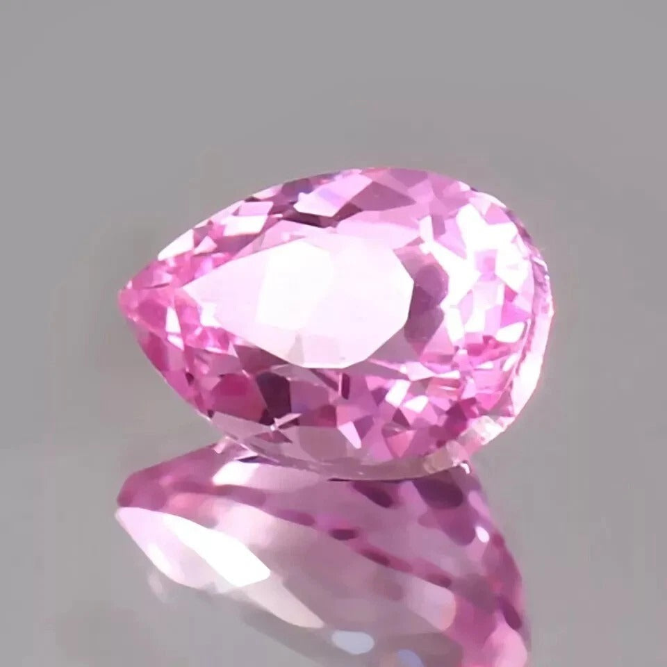 Pink Sapphire gemstone on a reflective surface with a gray background