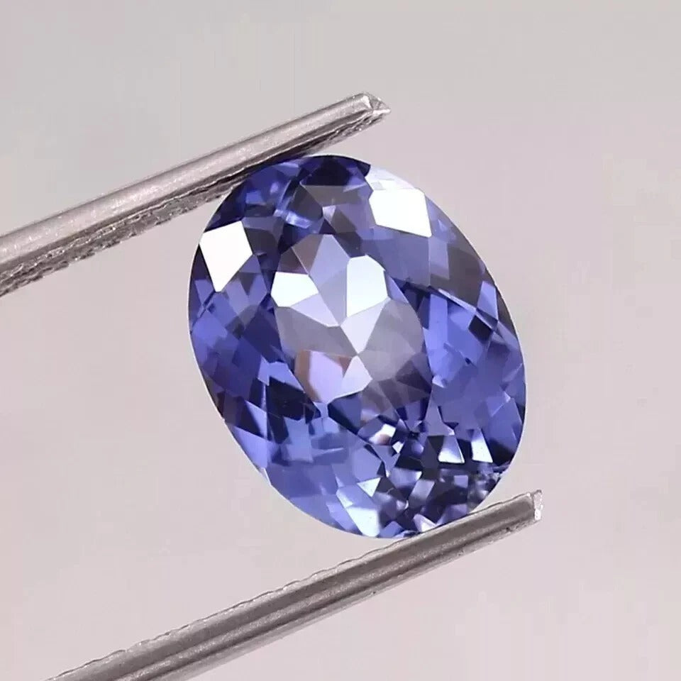 Faceted Blue Sapphire gemstone held between tweezers on a light gray background