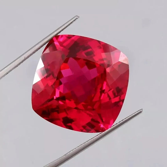 Blood Red Ruby gemstone held between tweezers on a light gray background