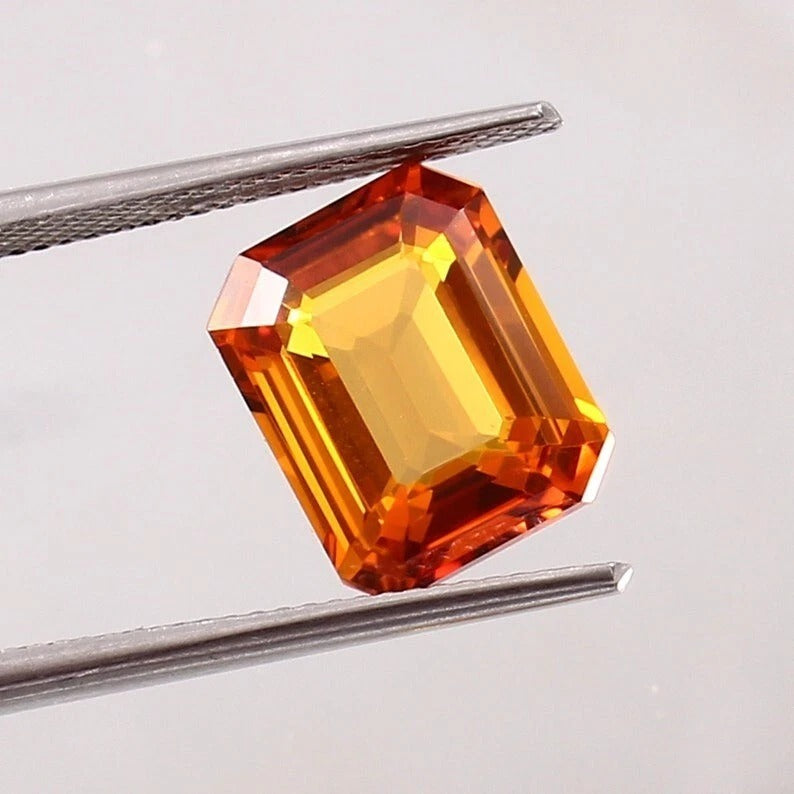 Orange Sapphire gemstone held between tweezers on a light gray background