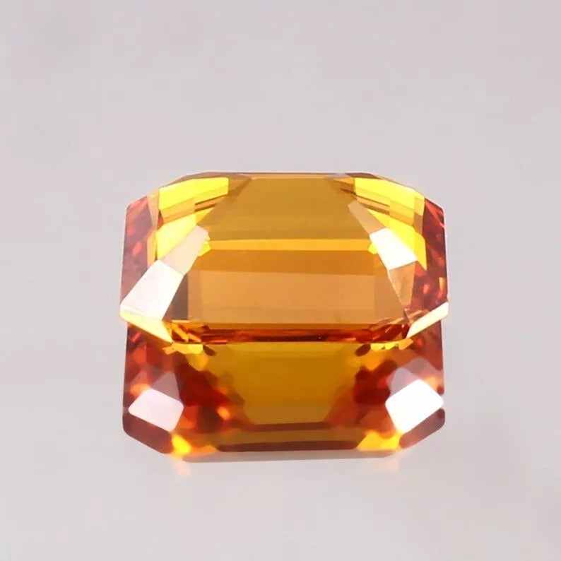 Orange Sapphire gemstone with orange and yellow hues on a light gray background