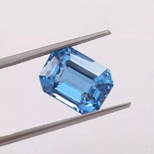 Blue Aquamarine gemstone held by tweezers on a light gray background