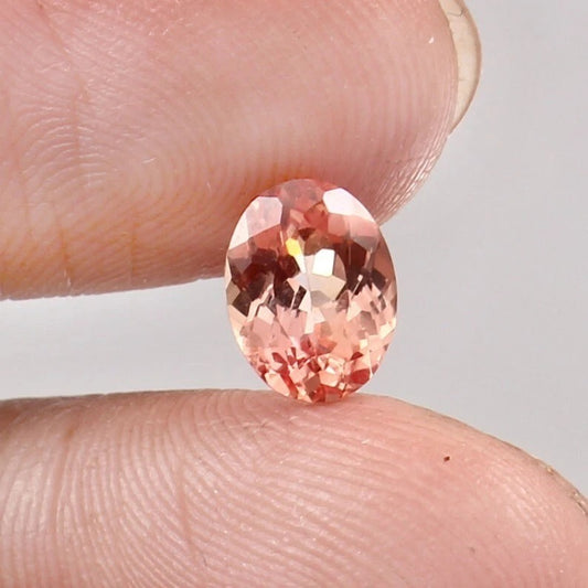Padparadscha Sapphire gemstone held between two fingers against a neutral background