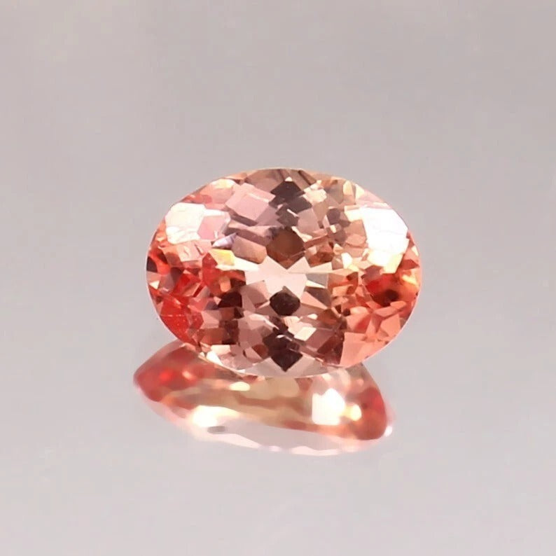 Oval-shaped Padparadscha Sapphire gemstone on a gray background