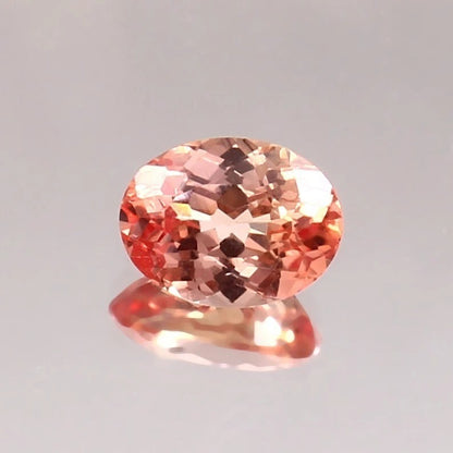Oval-shaped Padparadscha Sapphire gemstone on a gray background