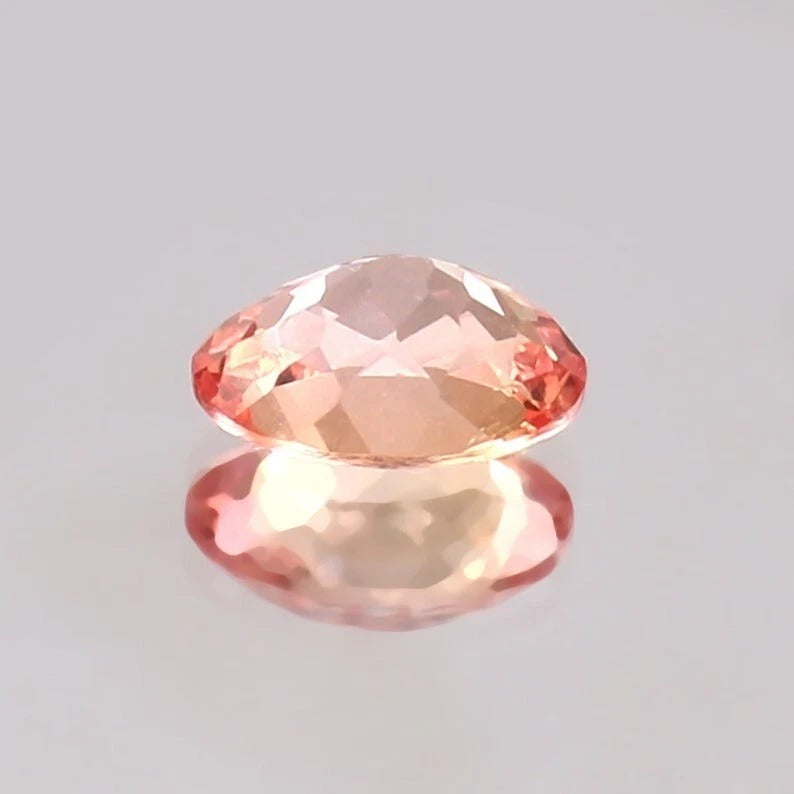 Faceted Padparadscha Sapphire gemstone on a gray background