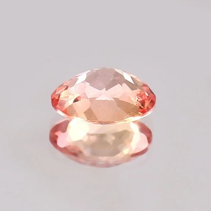 Faceted Padparadscha Sapphire gemstone on a gray background
