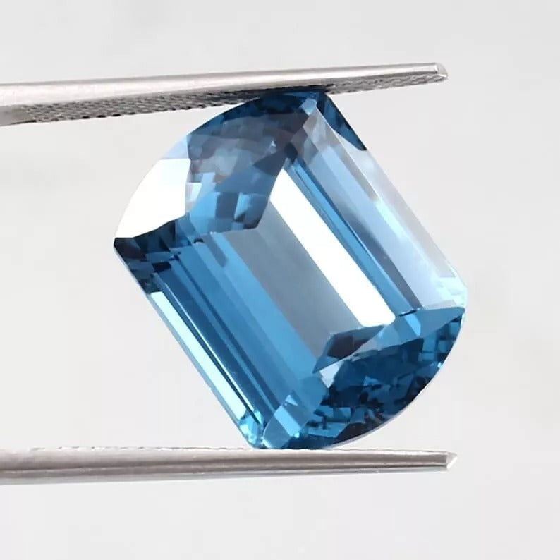 Blue Brazilian Aquamarine gemstone held by tweezers on a light gray background
