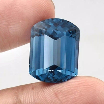 Blue Brazilian Aquamarine gemstone held between two fingers against a white background