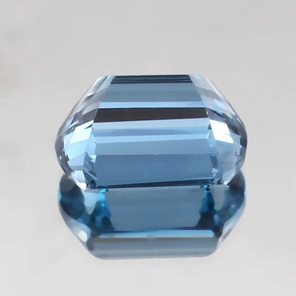 Faceted Brazilian Aquamarine gemstone on a reflective surface with a neutral background