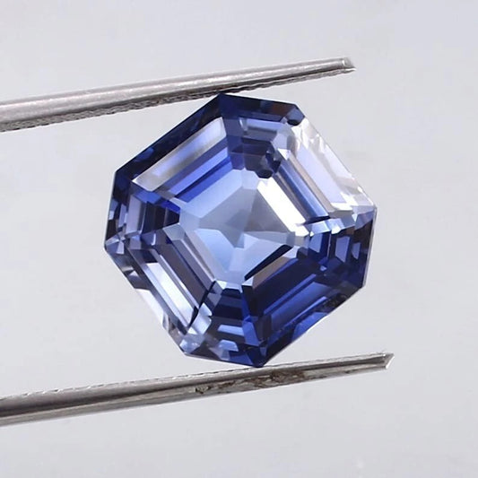 Cornflower Blue Sapphire gemstone held by tweezers on a light gray background