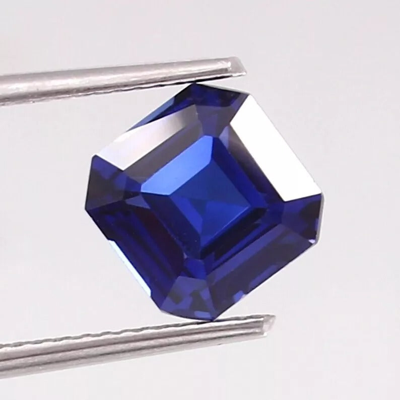 Cornflower blue sapphire gemstone with tweezers on a light gray background