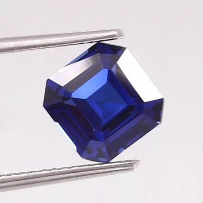 Cornflower blue sapphire gemstone with tweezers on a light gray background