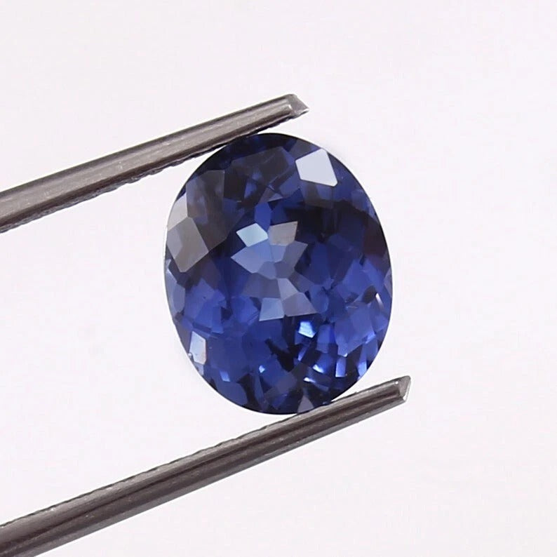 Royal Blue Sapphire gemstone held between tweezers on a white background